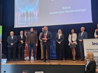 Przedstawiciele instytucji na scenie targów pracy, z ekranem prezentującym rektora UJW.