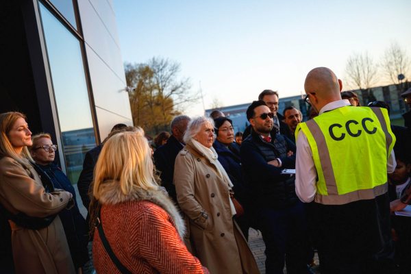Grupa uczestników słucha pracownika CCC przy przeszklonej fasadzie.