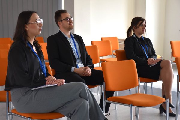 Troje uczestników z identyfikatorami siedzi na pomarańczowych krzesłach.