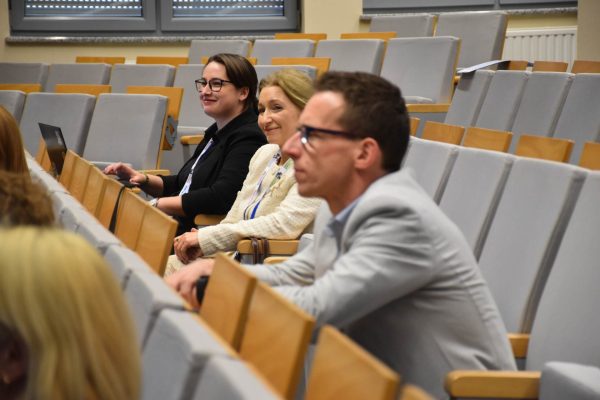 Uczestniczki konferencji uśmiechają się na widowni, jedna korzysta z laptopa.