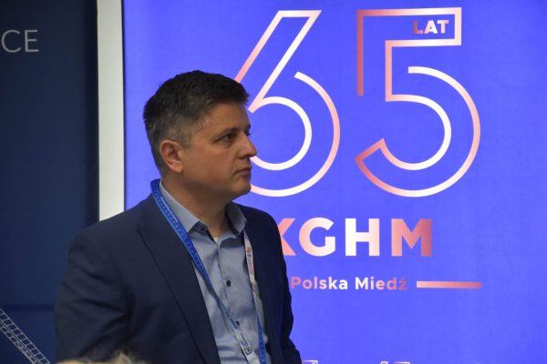 Uczestnik z identyfikatorem na tle planszy 65-lecia KGHM.