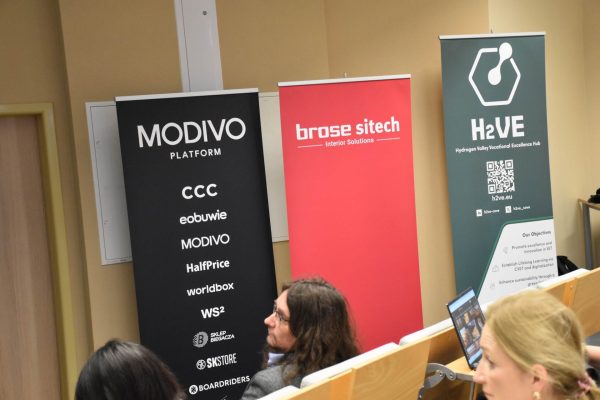Roll-upy MODIVO, Brose Sitech i projektu H2VE przy widowni konferencji.