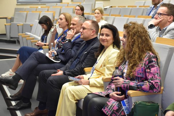Uczestnicy konferencji siedzą w fotelach, rozmawiając i uśmiechając się.