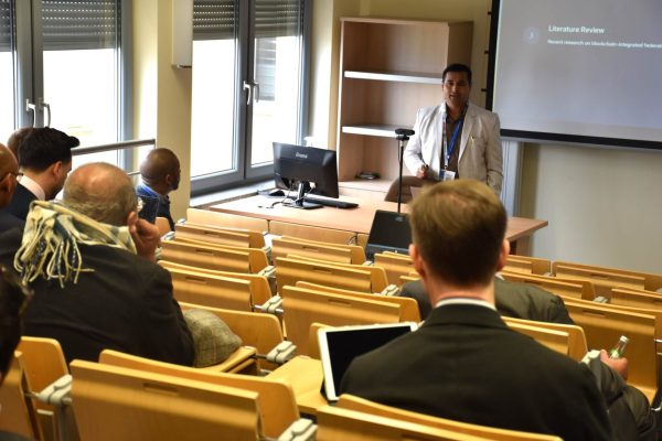 Prelegent w jasnej marynarce prowadzi prezentację przed publicznością.