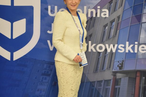 Uczestniczka w jasnym kostiumie pozuje na tle ścianki UJW.