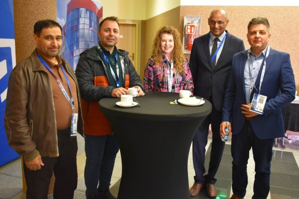 Pięcioro uczestników konferencji pozuje przy wysokim stoliku z filiżankami.