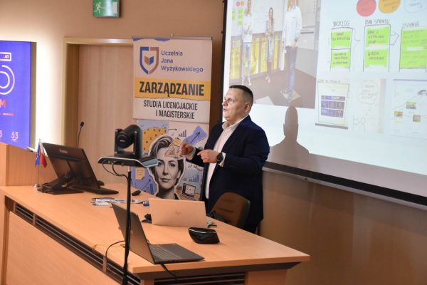 Prelegent omawia slajd ze schematami i przykładami organizacji pracy.