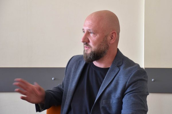 Mężczyzna w szarej marynarce gestykuluje podczas spotkania Klubu Absolwenta.