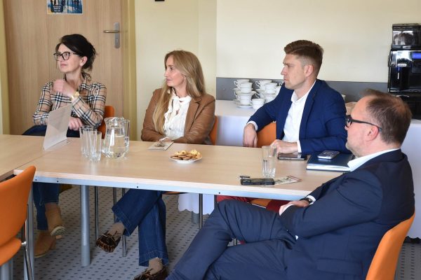 Uczestnicy spotkania słuchają wypowiedzi kobiety w marynarce w kratę.