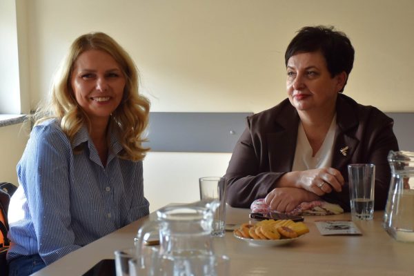 Dwie uczestniczki rozmawiają przy stole z poczęstunkiem.