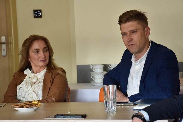 Kobieta w brązowej marynarce i mężczyzna w granatowym garniturze przy stole.