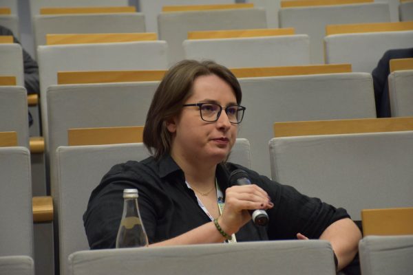Uczestniczka w okularach zabiera głos przez mikrofon z miejsca na widowni.