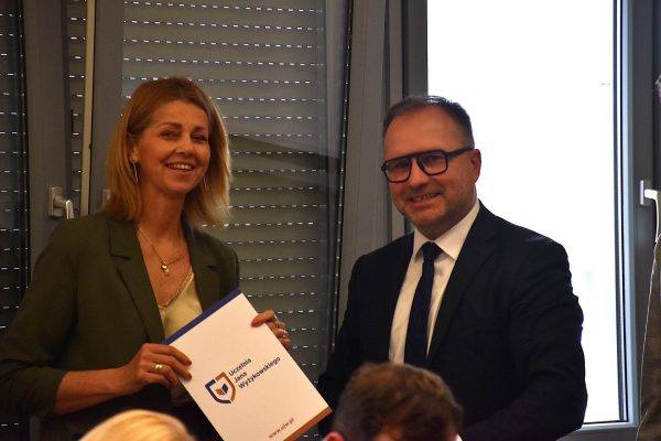 Uczestniczka w zielonej marynarce i mężczyzna w garniturze pozują z teczką UJW.
