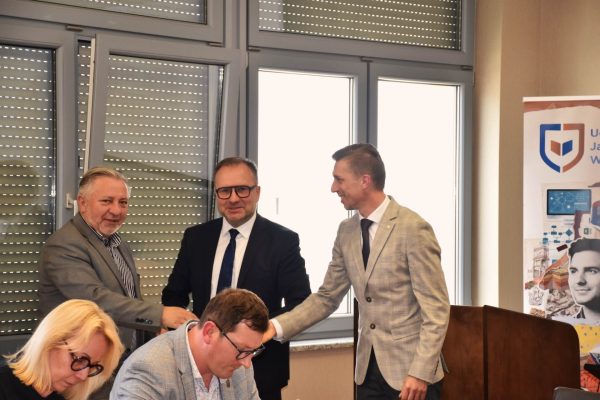Uczestnicy posiedzenia witają się uściskiem dłoni przy stole.