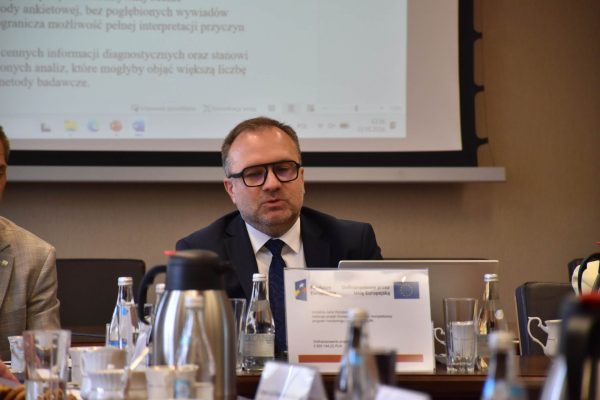 Uczestnik w okularach przemawia przy laptopie podczas posiedzenia.