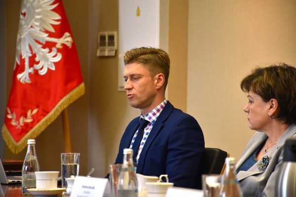 Mężczyzna w granatowej marynarce zabiera głos, obok siedzi uczestniczka posiedzenia.