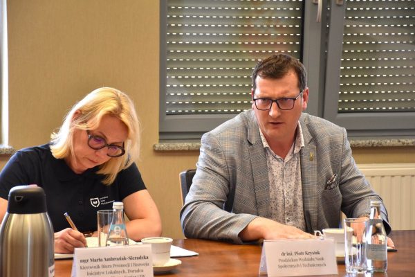 Uczestniczka notuje, a siedzący obok mężczyzna wypowiada się przy stole.