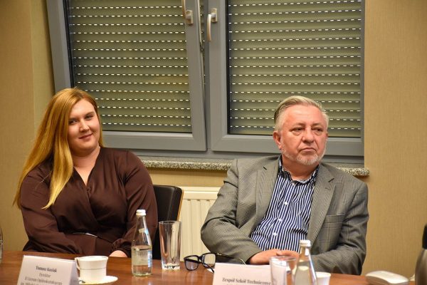 Dwoje uczestników posiedzenia słucha dyskusji pod oknem.