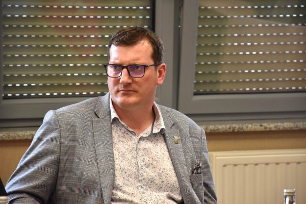 Mężczyzna w okularach i marynarce w kratę podczas posiedzenia.