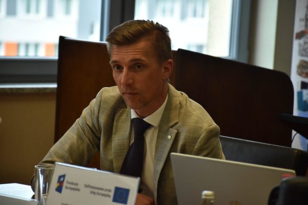 Uczestnik w jasnej marynarce przy dokumentach i laptopie.