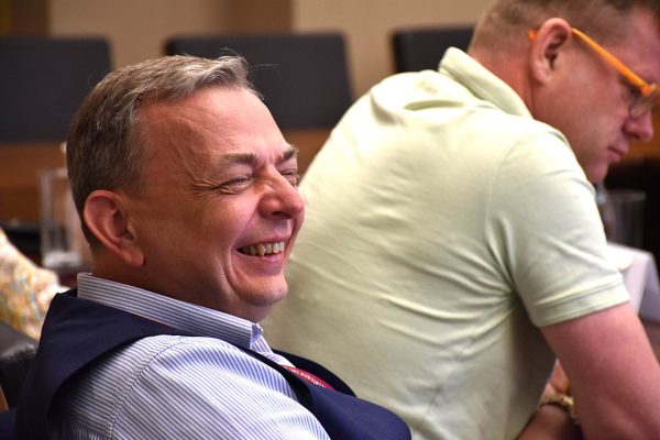 Uśmiechnięty uczestnik w kamizelce siedzi przy stole konferencyjnym.