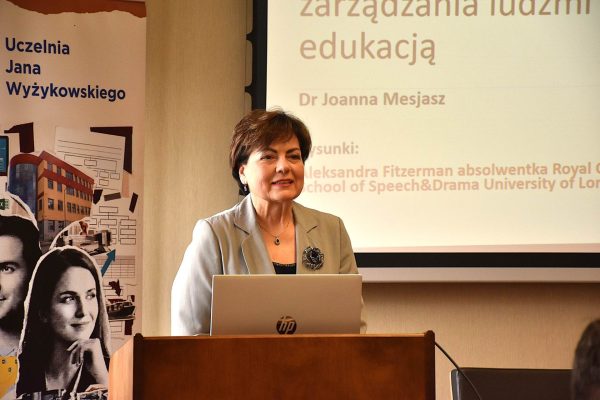 Prelegentka w szarej marynarce przy laptopie podczas prezentacji o neuroinkluzji.