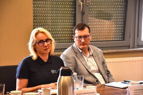 Dwoje uczestników słucha prezentacji przy stole konferencyjnym.