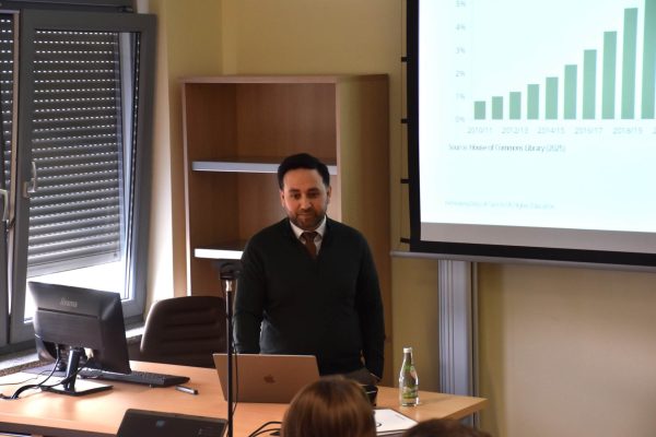 Prelegent przy laptopie na tle rosnącego wykresu słupkowego.