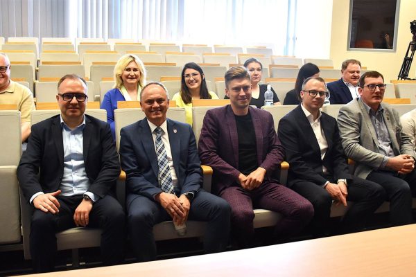 Uśmiechnięci uczestnicy konferencji studenckiej siedzą w rzędach foteli.