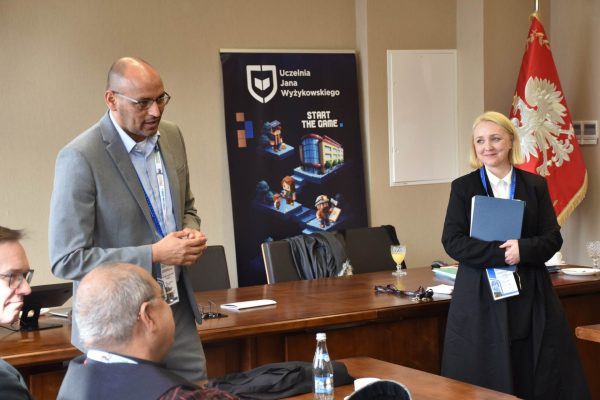 Mężczyzna w szarym garniturze i kobieta z teczką prowadzą spotkanie.