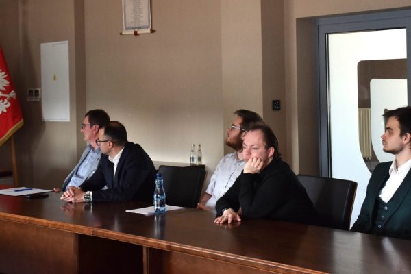 Uczestnicy konferencji siedzą przy drewnianym stole podczas prezentacji.