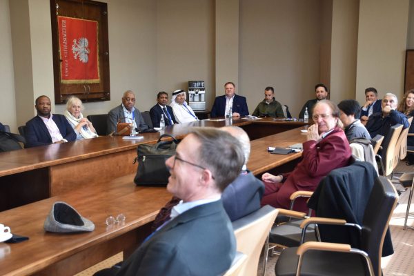 Szeroki widok uczestników spotkania przy stołach ustawionych w podkowę.