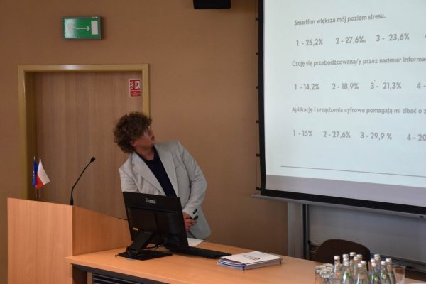 Prelegent analizuje slajd z wynikami ankiety o stresie i nadmiarze informacji.