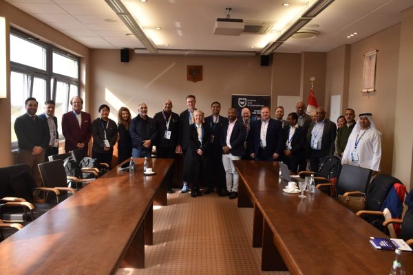 Grupowe zdjęcie uczestników konferencji w sali z drewnianymi stołami.