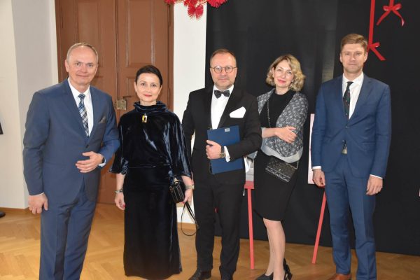 Pięcioro gości uroczystej kolacji pozuje w eleganckich strojach.