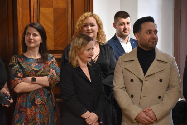 Uczestnicy gali obserwują wystąpienie, stojąc przy drewnianych drzwiach.