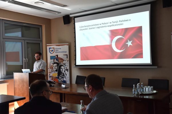 Prelegent przedstawia cyberbezpieczeństwo w Polsce i Turcji na tle flag obu państw.