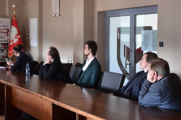 Uczestnicy konferencji studenckiej słuchają prezentacji przy stole.