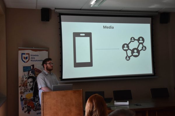 Prelegent omawia slajd „Media” z ikoną telefonu i sieci kontaktów.