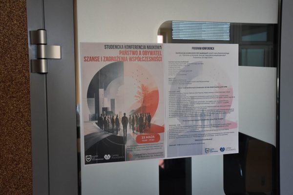 Plakat i program konferencji „Państwo a obywatel” na przeszklonych drzwiach.