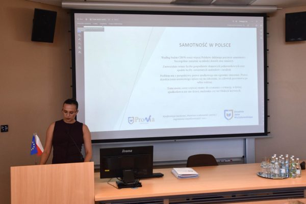Prelegentka przy mównicy omawia slajd „Samotność w Polsce”.