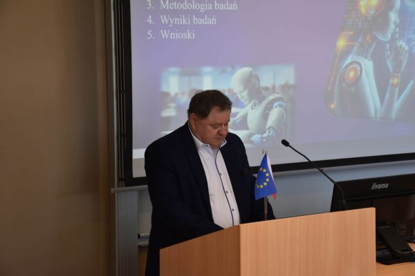 Prelegent odczytuje tekst przy mównicy na tle planu wystąpienia.