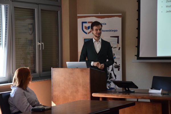 Prelegent w zielonym garniturze przy mównicy podczas konferencji studenckiej.