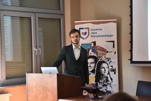Mężczyzna w zielonym garniturze zwraca się do publiczności.