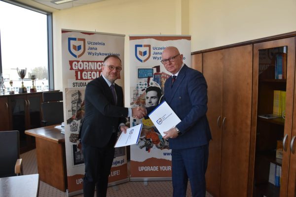 Przedstawiciele uczelni i szkoły ściskają dłonie, trzymając teczki z dokumentami.