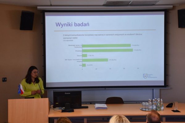 Prelegentka w zielonej bluzce prezentuje wyniki badań na wykresie.