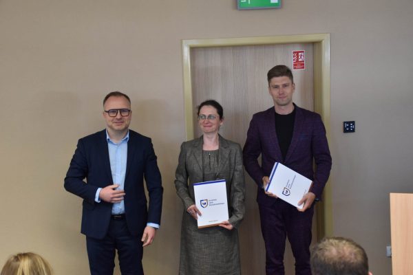Uczestniczka konferencji prezentuje dokument między dwoma organizatorami.