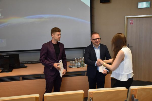 Wręczenie dokumentu uczestniczce w białej bluzce.