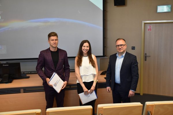 Uczestniczka w białej bluzce pozuje z organizatorami konferencji.