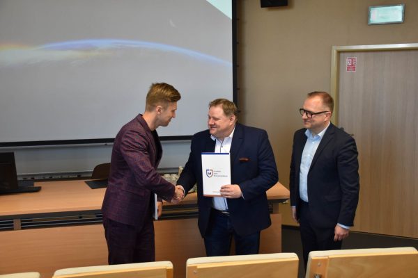Uścisk dłoni podczas wręczania dokumentu uczestnikowi konferencji.